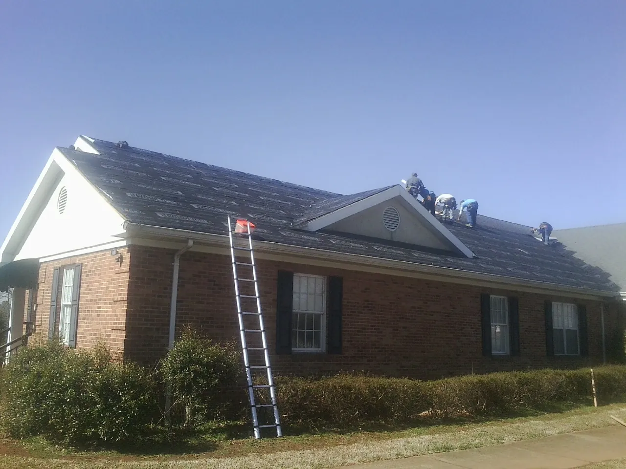 Crew tearing shingles off a brick ranch roof with a ladder set — Metal Roof Repair work by our crew in Providence Forge