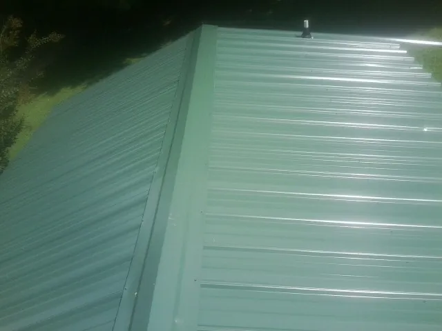 New green metal panels meeting at the ridge of a roof — Flat Roof Repair work by our crew in Providence Forge