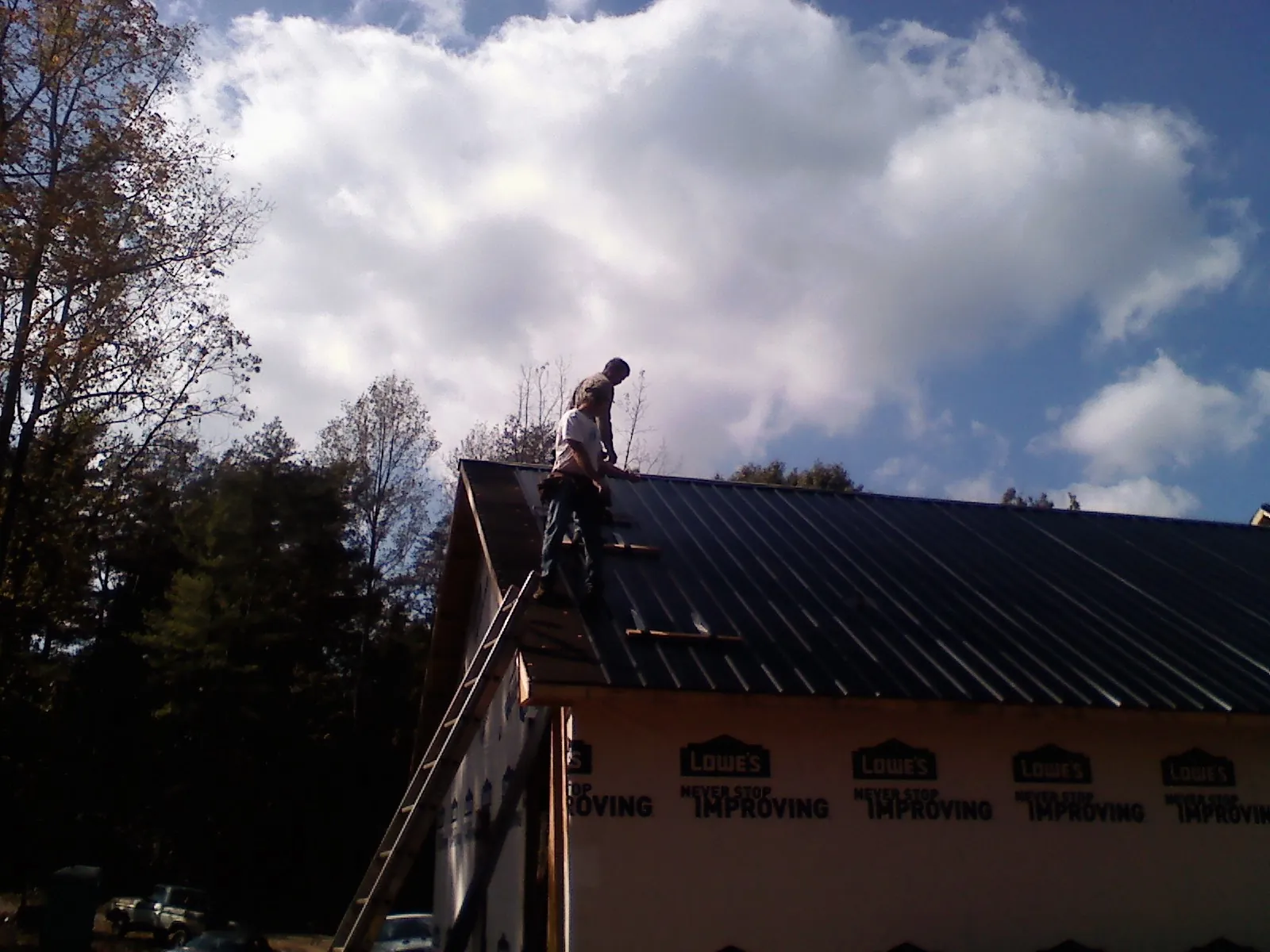 Roofer fastening dark metal panels high against a cloudy sky, from a Roof Inspection job in Providence Forge