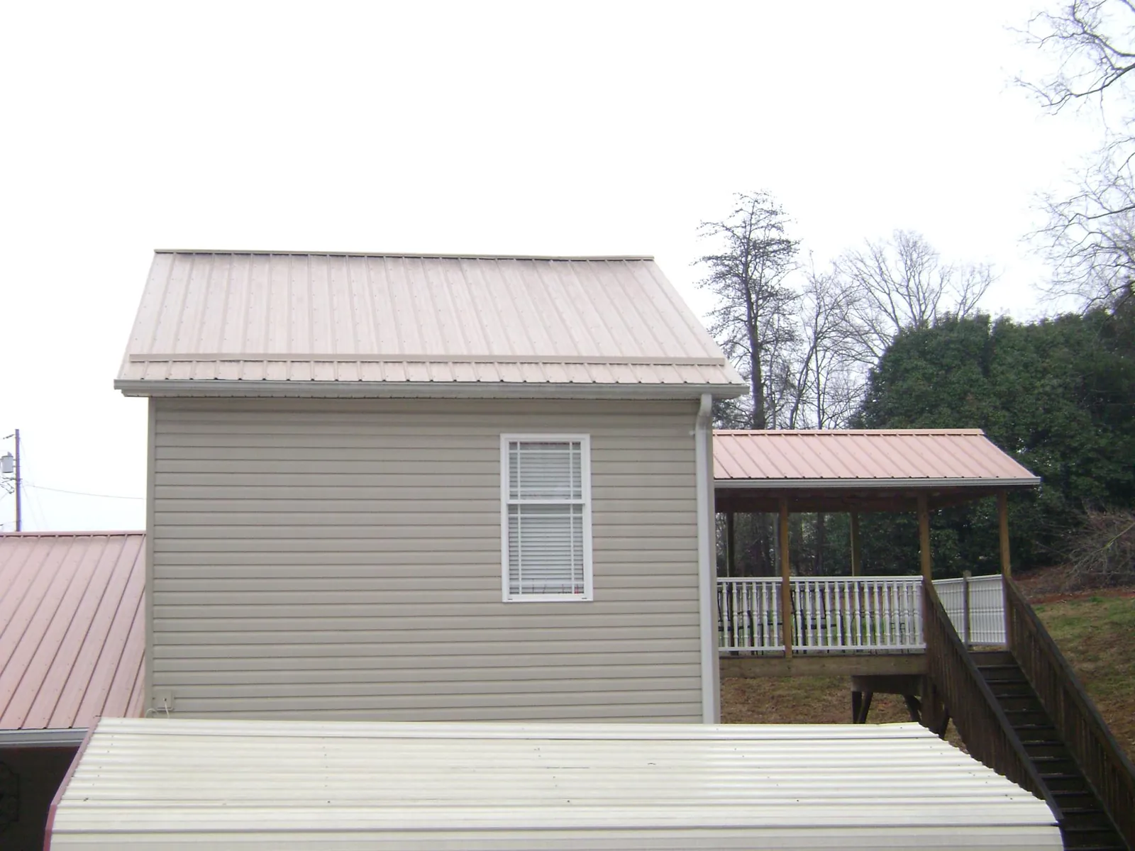 Tan metal roofs on a two story addition and attached porch, from a Roof Replacement job in Providence Forge